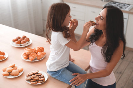 overhead view of woman and daughter feeding each other with cookies on the kitchenの写真素材