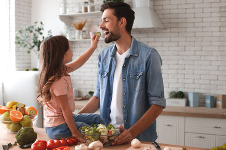 daughter and father tasting freshly cooked salad on the kitchenの写真素材