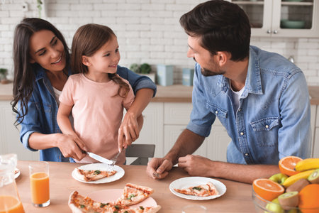 woman helping daughter with cutlery while father looking at them in the kitchenの写真素材