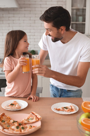 father clicking glasses with orange juice with daughter in the kitchenの写真素材