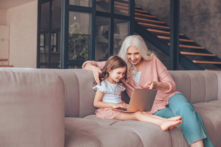 grandmother and granddaughter sitting on the couch and using laptop at home