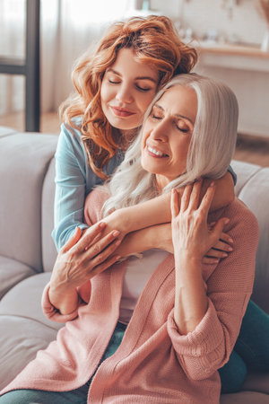 happy senior mother sitting on the couch and her daughter hugging her from the backの写真素材