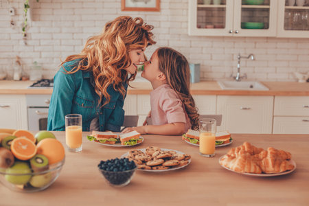 side view of daughter and mother touching noses while sitting at the kitchen table with foodの写真素材