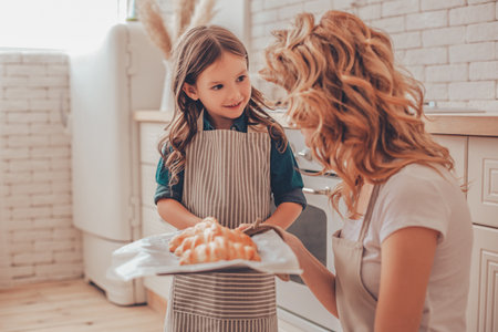 daughter and mother holding tray with croissants on the kitchenの写真素材