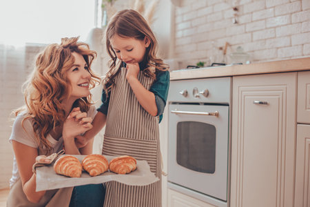 mother holding tray with freshly baked croissants while girl looking at themの写真素材