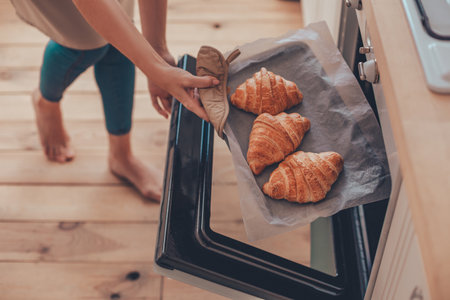 close up of woman hands taking out freshly baked croissants from the ovenの写真素材