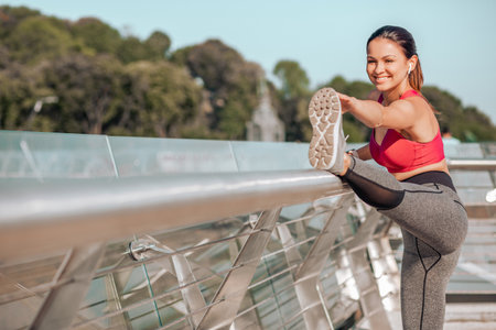 portrait of active woman warming legs while standing on the bridge in the city