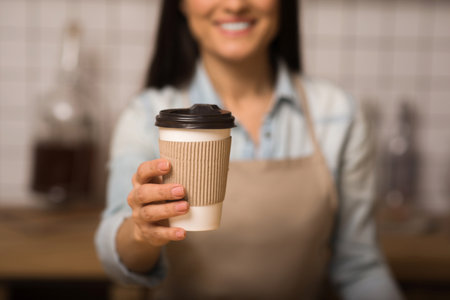cropped shot of waitress holding coffee to go in paper cup with blurred backgroundの写真素材