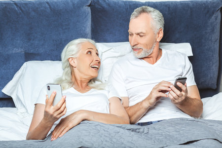portrait of senior couple using smartphones in the bed