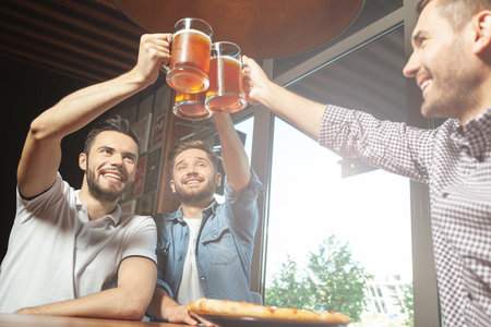 low angle view of men cheering with beer bottles in pubの写真素材