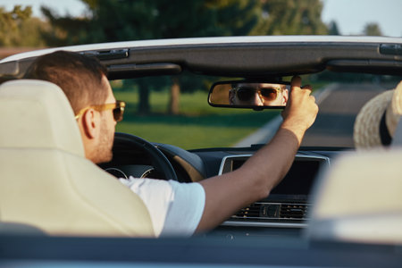 back view of man in sunglasses looking in the car mirror