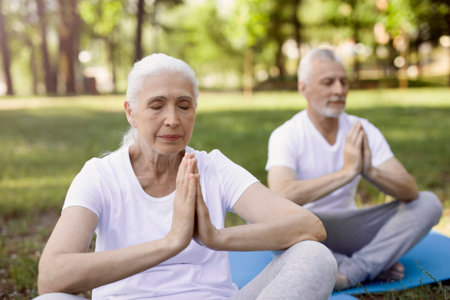 Calm elderly couple sitting in lotus pose with their palms together and eyes closedの写真素材
