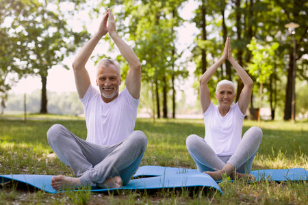 Positive senior couple keeping their hands up and crossing their legs while meditating togetherの写真素材