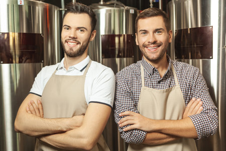two smiling workers wearing aprons with crossed hands looking at the camera at beer plantの写真素材