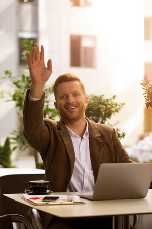 Friendly stylish man waving his hand for gaining waiters attention while sitting at the tableの写真素材