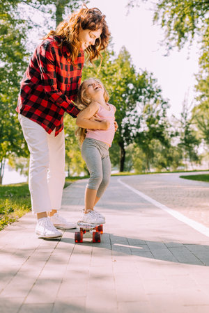 mother teaching daughter riding skateboard in the park, full length shotの写真素材