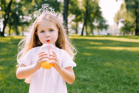 portrait of cute girl with curly hair drinking orange juice in the park an looking at the cameraの写真素材