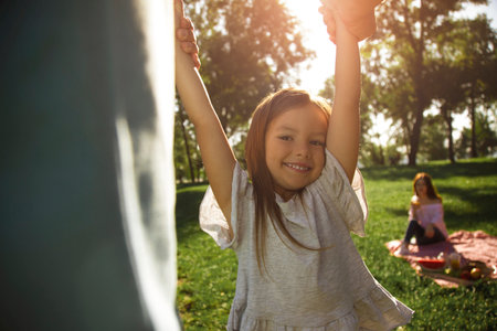 father playing with daughter with mother on the background in the parkの写真素材