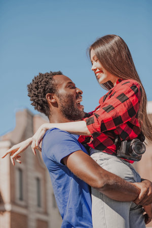 young man holding happy woman on the hands and looking at each other outdoors