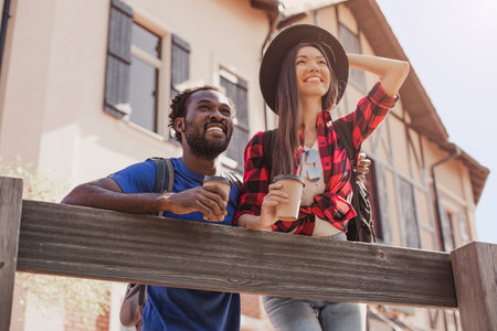 female and male tourists standing at wooden fence at the river looking away with coffee cupsの写真素材