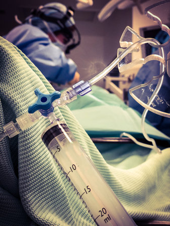 View of surgeon in the background - selective focus - with syringe and intravenous line in the foreground.の写真素材