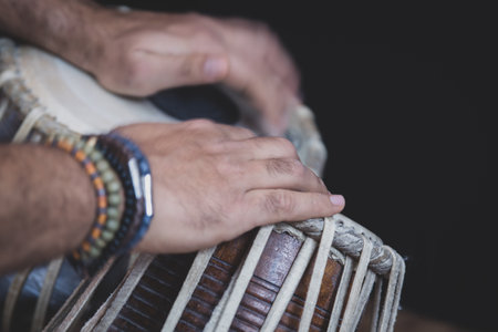 Images of a man's hands (wearing beads) playing the Tabla - Indian classical music percussion instrument - black background.の写真素材