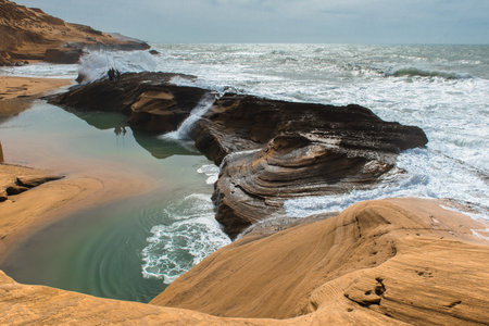 Fishirmen and waves rolling over the rocks into cove, Atlantic coast of Moroccoの写真素材