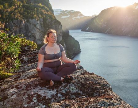 Mindful overweight female practicing yoga outdoors, finding peace and tranquility in wilderness with beautiful scenic viewの素材
