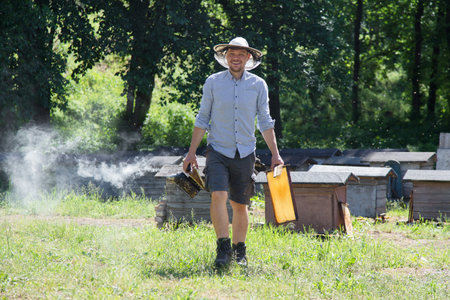 Beekeeper at work by the wooden bee hives. Young farmer in his farm.