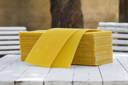 Plates of wax foundation - stack of apiary honeycomb base elements on wooden table.の写真素材