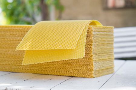 Plates of wax foundation - stack of apiary honeycomb base elements on wooden table.の写真素材