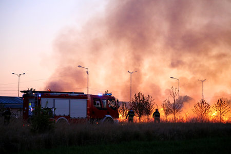 Team of fire fighters fighting fire in the evening. Fire truck on the flames and smoke background.