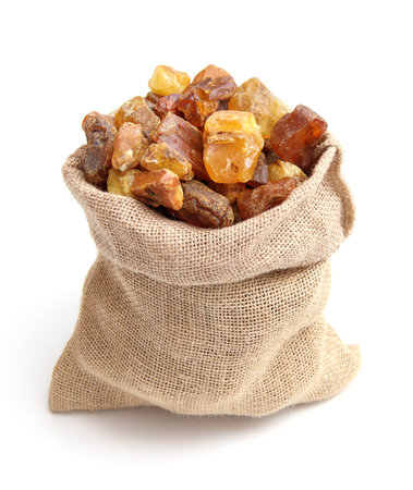 Natural raw amber jute bag isolated on white background. Multiple amber gemstone in various shapes and color gathered in bag. Jewelry components.の写真素材