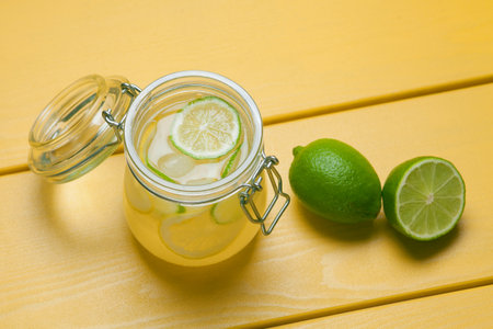 Lemonade with ice, lemon and lime in a jar on a yellow wooden background. Summer drink.の写真素材