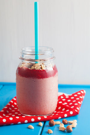 Healthy pink smoothie made from strawberries and banana with nuts in a jar with a blue straw on a blue wooden table.の写真素材