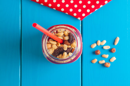 Healthy pink smoothie made from strawberries and banana with nuts in a jar with a blue straw on a...