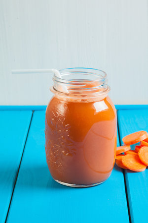 Healthy carrot apple smoothie in a jar on blue wooden background. Vegetable drink.の写真素材