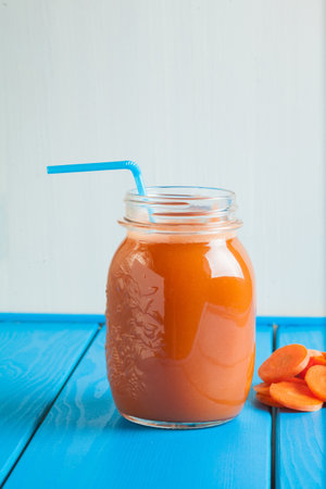 Healthy carrot smoothie in a jar on blue wooden background. Vegetable drink.の写真素材