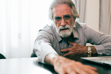 Senior man holding hand on chest and suffering from heart problem at homeの写真素材