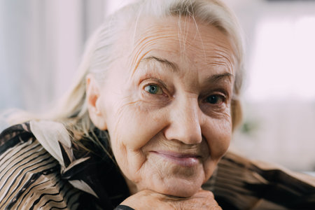 Smiling portrait of happy senior woman smiling and sitting on sofa at homeの写真素材