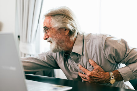 Senior man holding hand on chest and suffering from heart problem at home