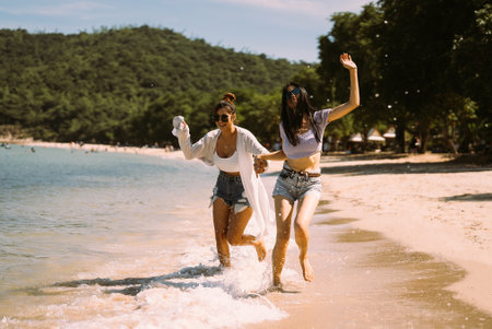 Portrait of two young female friends walking on sea shore happilyの写真素材