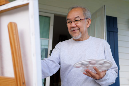 Senior man holding color paint drawing on white paper at homeの写真素材