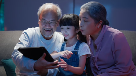 Granddaughter using tablet with senior grandfather and grandmother at homeの写真素材