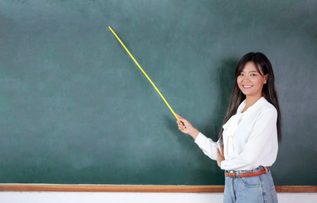 Teacher standing near backboard holding textbook posing to camera with smileの写真素材