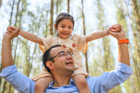 Happy father giving daughter piggyback ride on his shoulder in parkの写真素材
