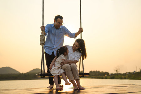 Family enjoying with outdoor activities sitting on swing with sunsetの写真素材