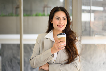 Smiling portrait of beautiful businesswoman with cup of coffee in officeの写真素材