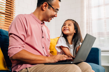 Father using laptop playing with daughter in living roomの写真素材