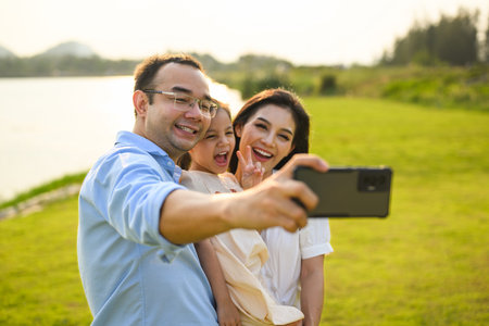 Family taking selfie photo together with green meadow and river viewの写真素材